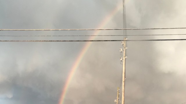 A rainbow arc behind power lines.