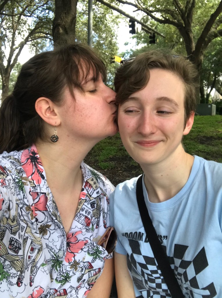 Me kissing my partner on the cheek at a park.